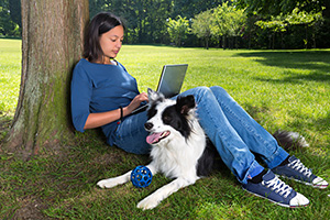 woman with laptop and dog under tree